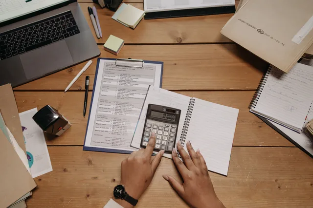 Hands working with calculator and documents on wooden desk in office setting. Placing clients into tax preparation services packages